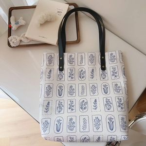 Top view of canvas tote bag with blue floral print and premium black leather handles