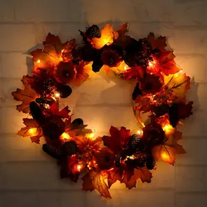 Lighted autumn wreath with artificial maple leaves, pumpkins and pine cones on white wall