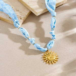 Detail of silk ribbon necklace with gold sun face pendant on elegant stone decor