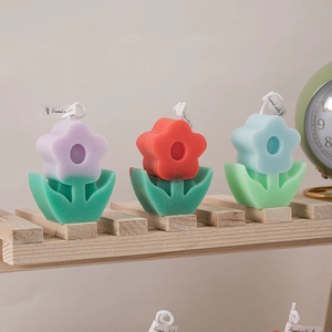 Three flower-shaped scented candles in purple, red, and blue colors on a wooden tray