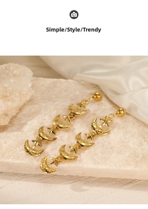 Close-up of long gold star and moon tassel earrings on a textured stone surface