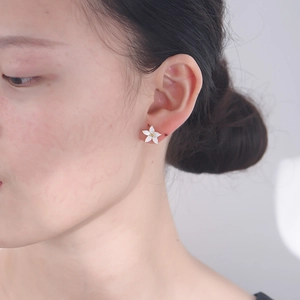 Close-up of elegant white five-petal flower stud earring with gold center worn by a model