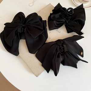 Three elegant black satin bow hair claws with silk texture on beige book background