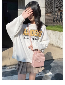 Pink quilted crossbody bag with plaid mini skirt and white sweatshirt in sunny outdoor setting