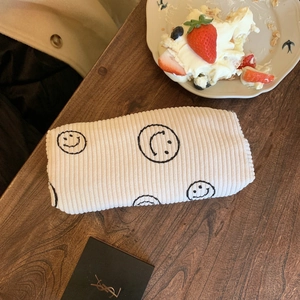 Corduroy makeup bag with black smiley face embroidery on a rustic wooden table