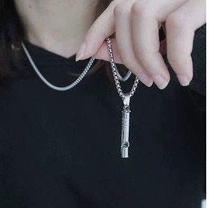 Detail of silver whistle pendant necklace with metallic finish shown on model clothes
