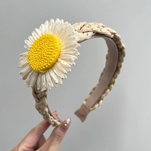 Close-up of woven straw headband featuring a large white daisy flower with yellow center
