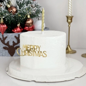 Golden Merry Christmas acrylic cake topper with matching candles on a white festive cake