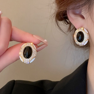 Close-up of vintage gold earrings with black gemstone, white enamel, and rhinestones
