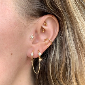 Detail of gold star and lightning stud earrings with chain link for multi-piercing