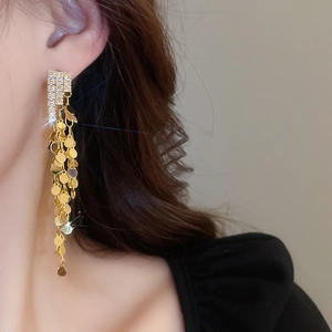 Close-up of long gold fringe earrings with sparkling zircon rhinestones on a female model