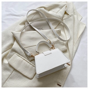 Detail view of white textured leather handbag with gold hardware on a neutral background