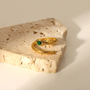 Close-up of 18K gold snake ring with green gemstone on a natural stone background