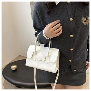 Detail view of the sleek white patent leather handbag with stitching on the flap