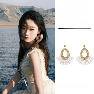 Detail of raffia fan earrings with white fringe tassels for bohemian vacation style