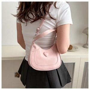 Pink PU leather crossbody bag with heart detail worn by a model in a natural home setting