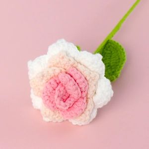 Close-up of handmade crochet rose with pink gradient petals and green stem on pink background
