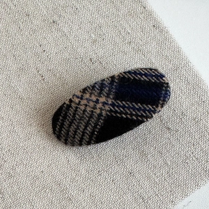 Detailed top view of plaid oval hair clip featuring vintage beige wool texture on linen