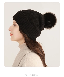 Detail showing the black knitted beanie with a large faux fur pompom and soft ribbed texture