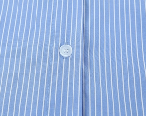 Detailed macro view of the blue striped cotton shirt featuring a clear round button detail