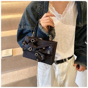 Detailed view of a black evening clutch bag with a rhinestone bow and gold chain strap