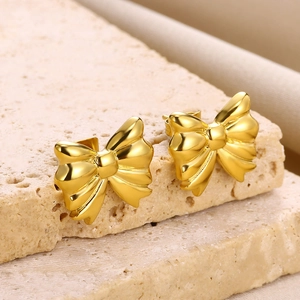 Macro shot of 18K gold bow stud earrings with polished mirror finish on beige stone