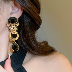 Close-up of golden leopard head earrings with black gemstone drop on a model