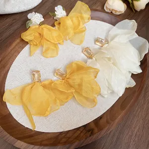 Handmade fabric flower earrings with zircon and yellow organza petals in a wooden tray
