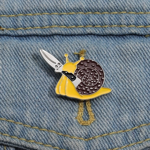 Close-up of yellow snail enamel pin with a knife on blue denim fabric texture