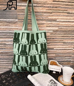 Detail of knitted tote bag featuring a green checkered pixelated rabbit pattern and strap