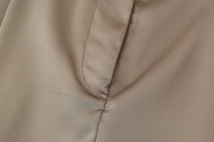 Detailed close-up of khaki satin wide-leg pants showing premium stitching and fabric texture