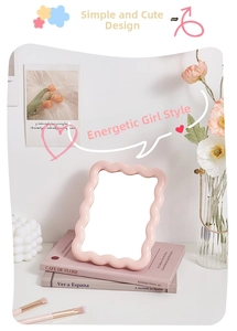 Detailed view of a pink wavy-edged desk makeup mirror with decorative lifestyle props