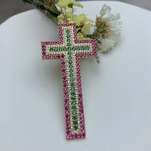 18k gold cross pendant with pink and green zircon stones on white ceramic tray