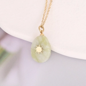 Detail of light green teardrop stone pendant with gold sun motif on a stainless steel chain