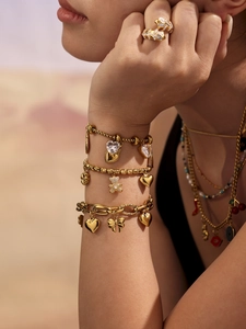 Detail of layered gold charm bracelets with teddy bear and heart pendants on wrist