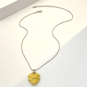 Macro-opname van gele hartvormige hanger met zilverdraad op een slanke slangenketting