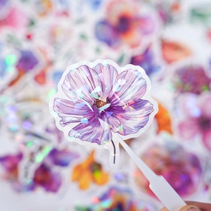 Macro shot of holographic purple flower sticker held with tweezers showing laser effect