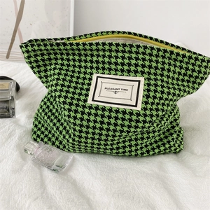 Close-up of green houndstooth makeup bag with yellow zipper and PLEASANT TIME label