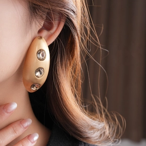 Close-up of golden brushed metal oval earrings with crystals worn by a model