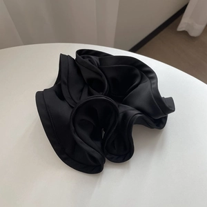 Detailed close-up of glossy black satin hair scrunchie with elegant ruffled texture