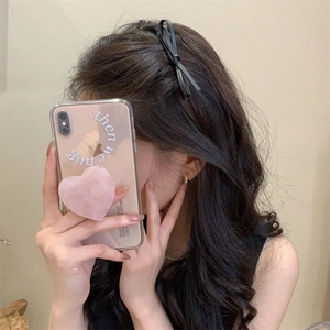 Close-up of lifestyle selfie showing black leather bow hair clip and pink heart phone case