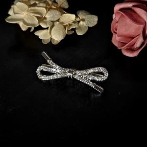 Macro shot of silver bow hair clip with sparkling rhinestones on black reflective surface