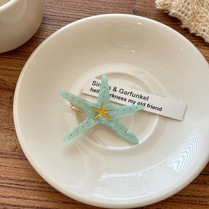 Close-up of a mint green starfish hair clip with gold speckles on a white ceramic plate