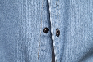 Détail de la chemise en jean délavé avec coutures orange et boutons-pression en métal