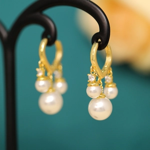 Macro shot of gold pearl tassel earrings with three white pearls and sparkling zircons