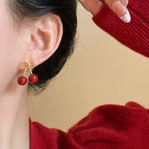Detail of red cherry earrings with gold bow on model wearing a red sweater