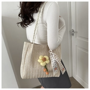 Detail of beige woven tote bag with yellow floral charm and printed silk scarf accessory