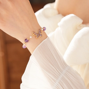 Close-up of golden butterfly bracelet featuring purple crystals and white pearls on wrist