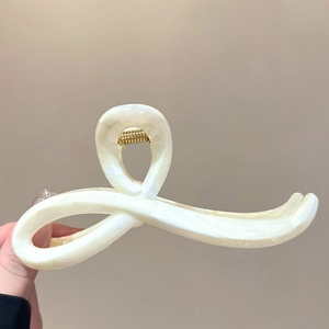 Detail shot of a creamy acrylic hair claw clip with a sleek twisted crossover design
