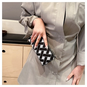 Close-up of a woven clutch bag with black and white geometric patterns and silver zipper